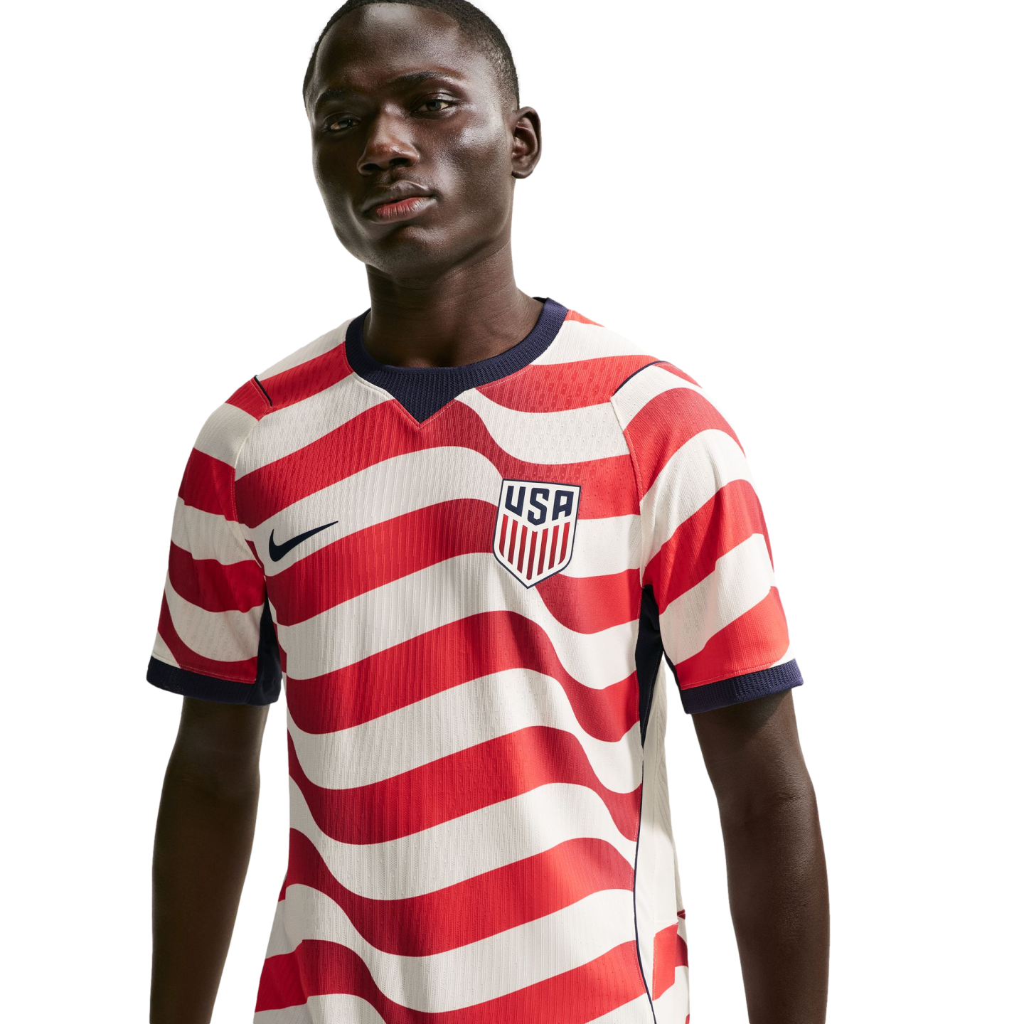 A man wearing a USA soccer jersey with red and white wavy stripes, featuring a Nike swoosh and USA crest, against a solid black background.