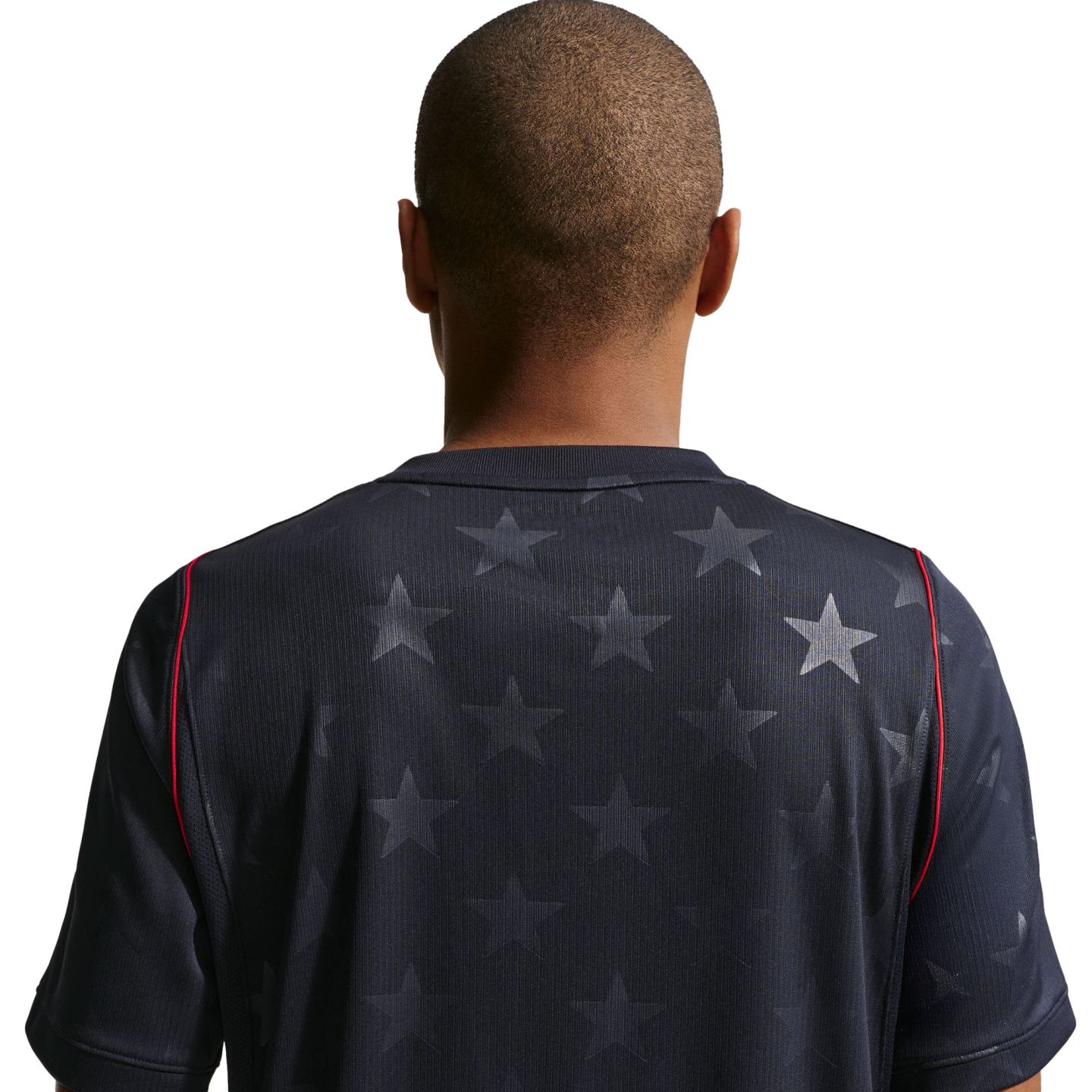 Back view of a man with a buzz cut wearing a navy blue jersey with a tonal star pattern and red shoulder piping, set against a black background.