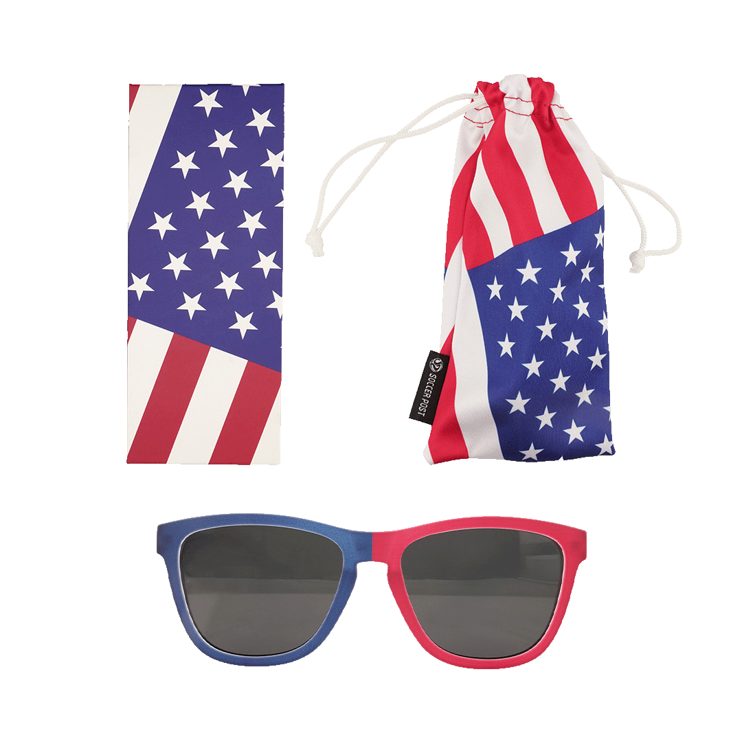 A set of American flag-themed accessories featuring patriotic red, white, and blue colors. The set includes a pair of sunglasses with one blue frame and one red frame, a rectangular cleaning cloth with a star and stripe pattern, and a matching soft drawstring pouch labeled with a "Soccer Post" tag.